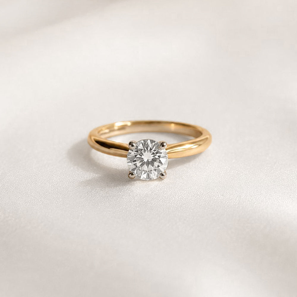 Gold ring with a 1ct round diamond on a light gray background