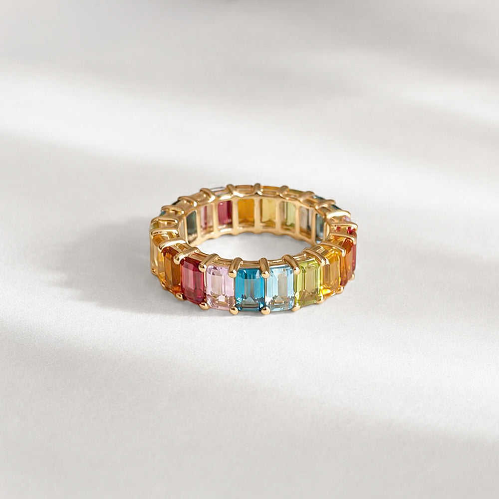 Gold ring with multicolored gemstones on a light gray background